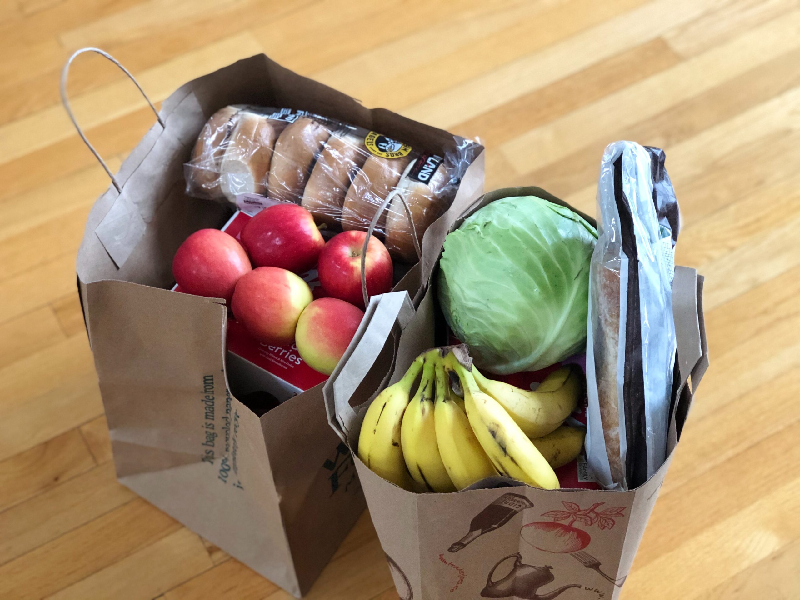 bag of groceries in paper bags on wooden floor to accompany a plant based grocery list