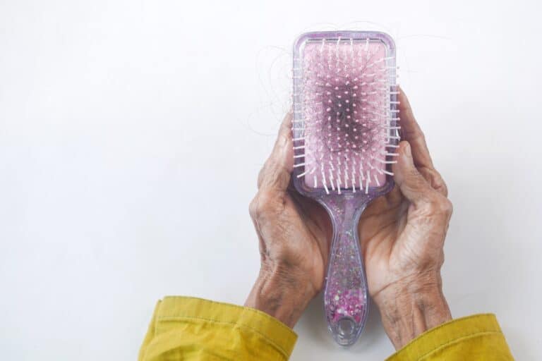 A rectangular hair brush with black hair in it on a white background. It is being cupped by the hands of a person wearing a yellow long sleeve shirt.
